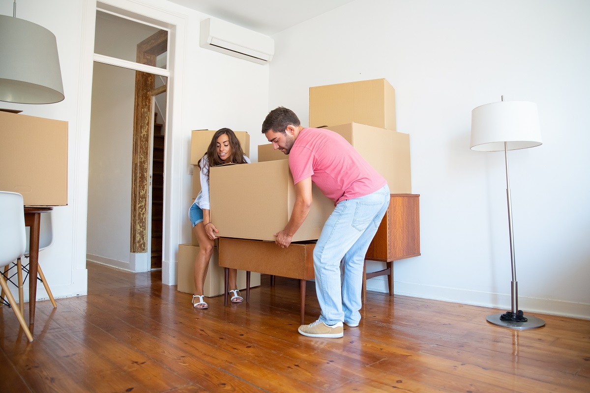 Jovem casal se mudando para um novo apartamento carregando caixas de papelão e móveis