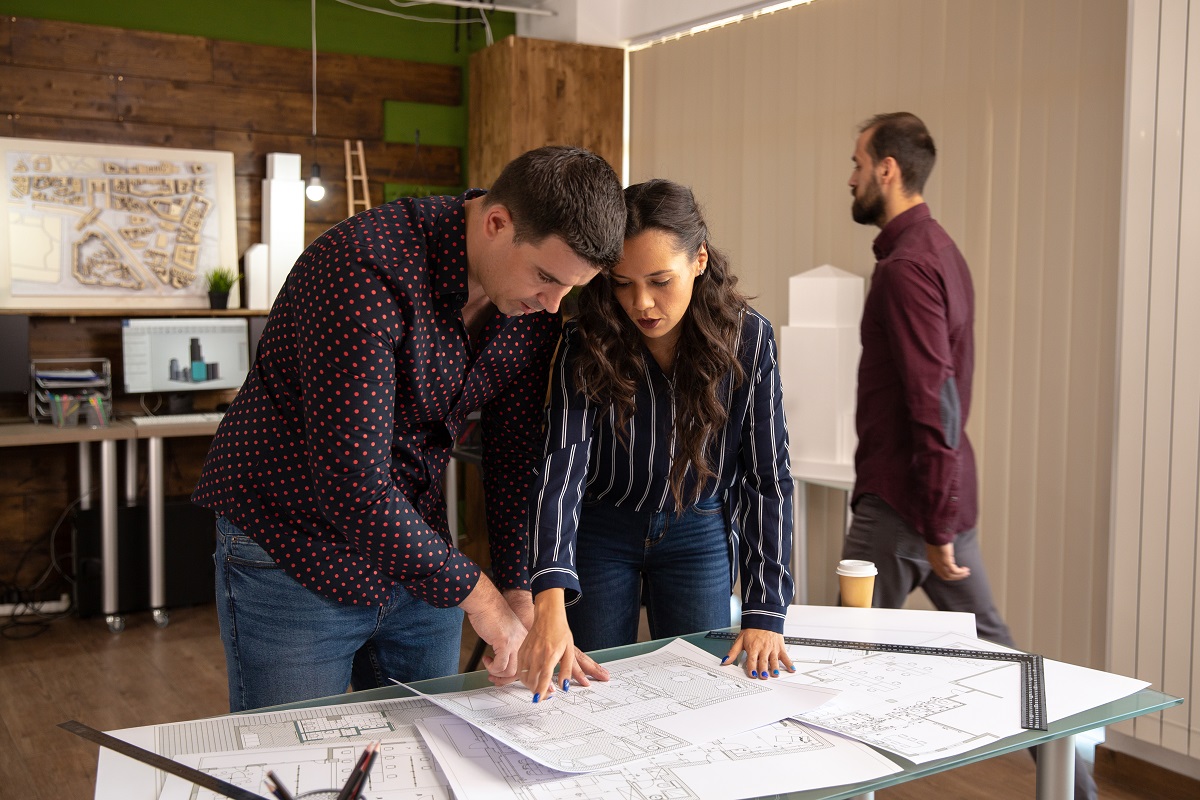 Dois colegas arquitetos em pé da mesa discutindo projeto